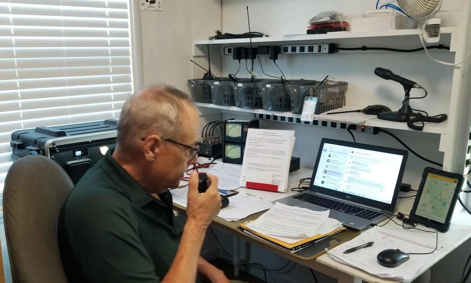 Man using a radio transceiver in a cluttered home office with multiple devices.